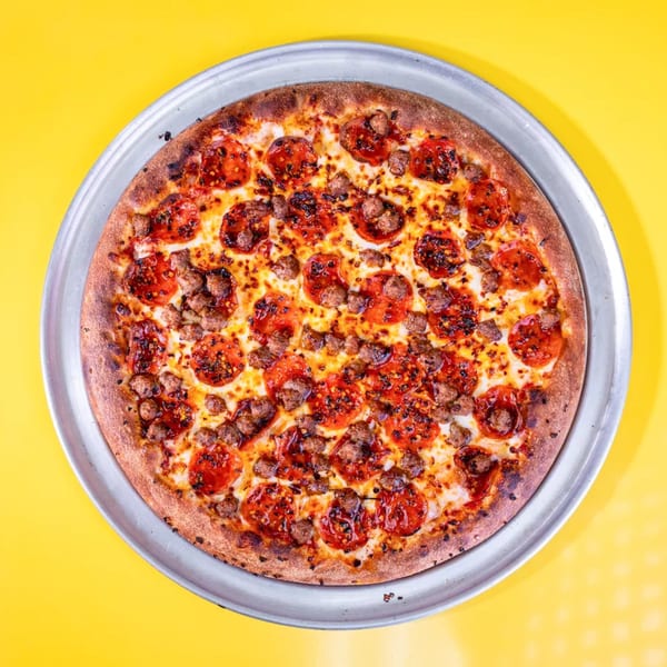 A whole pepperoni and sausage pizza on a metal pan against a bright yellow background.