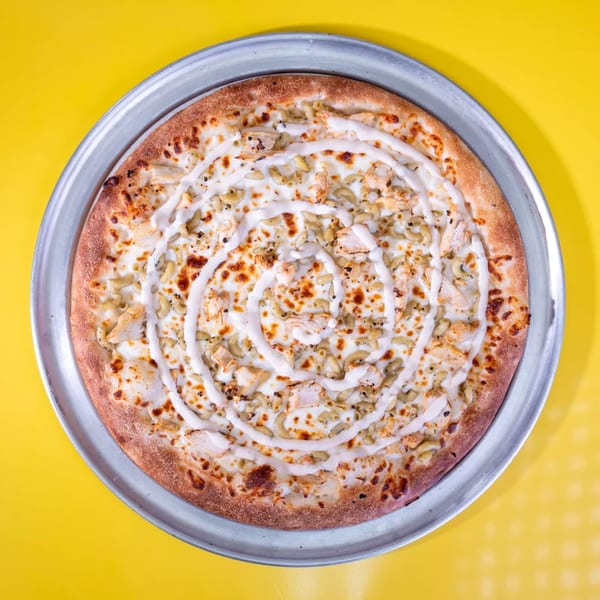 Overhead view of a mac and cheese pizza with chicken and white sauce drizzle on a metal pan.