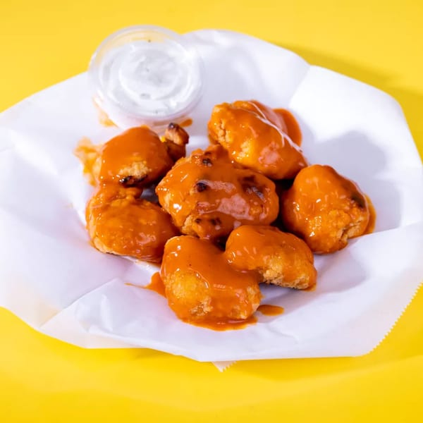 Seven boneless chicken wings coated in orange sauce, with a side of ranch dressing, on a yellow background.