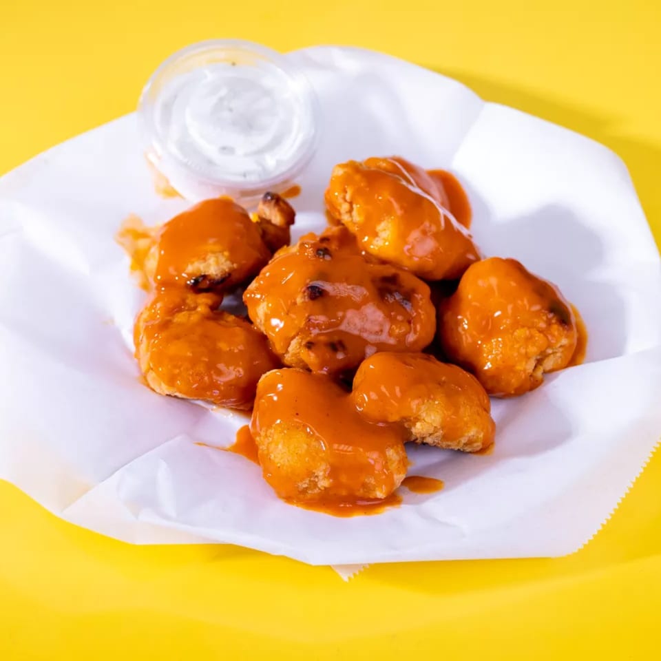 Seven boneless chicken wings coated in orange sauce, with a side of ranch dressing, on a yellow background.