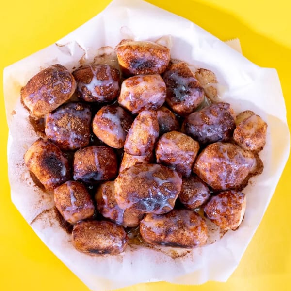 A pile of cinnamon sugar donut holes with white icing drizzle, served in a paper-lined basket.
