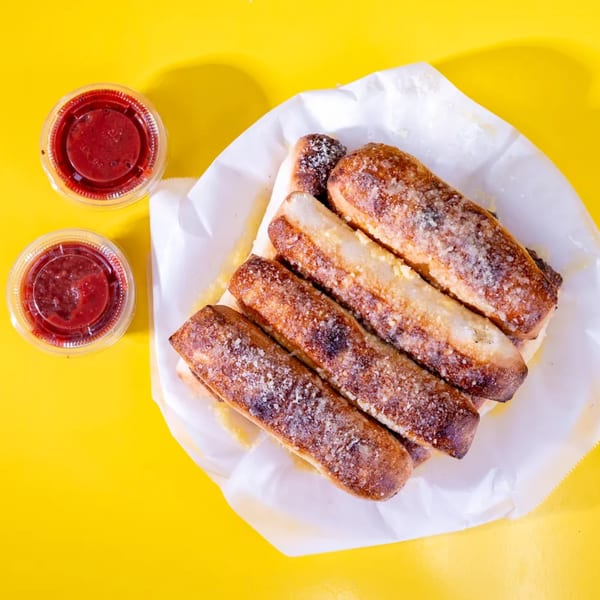 Top-down view of five golden-brown breadsticks with parmesan cheese, served with two cups of marinara sauce.