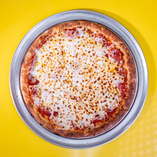 A whole pepperoni pizza with melted cheese on a metal pan, centered on a bright yellow background.