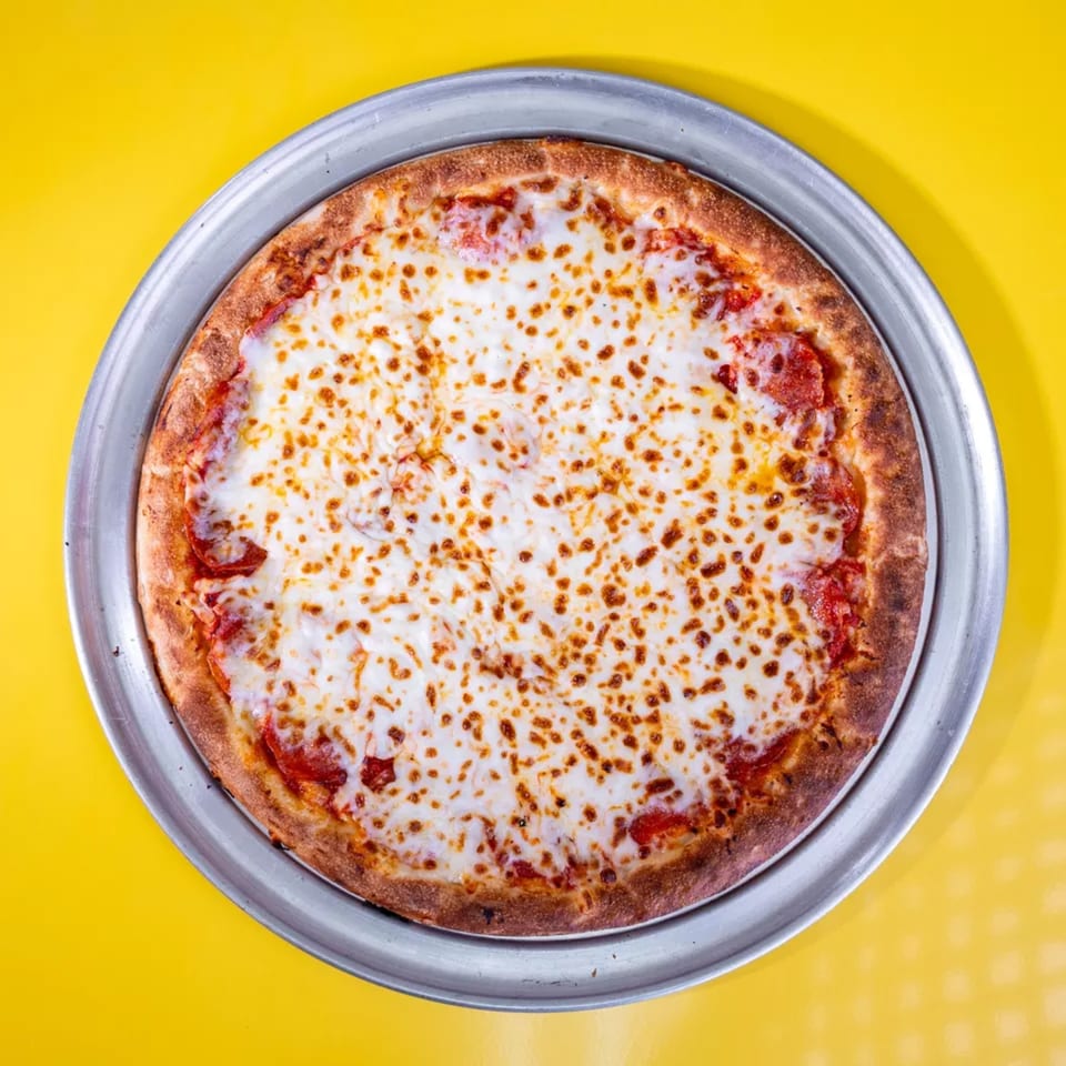 A whole pepperoni pizza with melted cheese on a metal pan, centered on a bright yellow background.