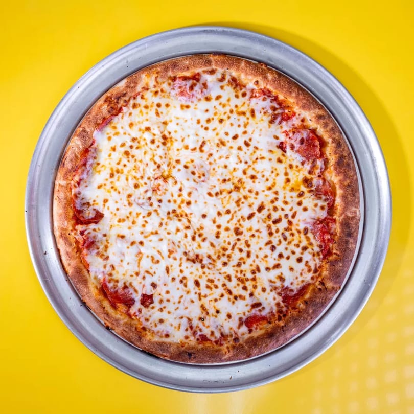 A whole pepperoni pizza with melted cheese on a metal pan, centered on a bright yellow background.