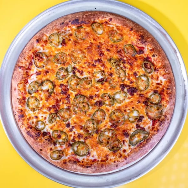 A whole round pizza with melted cheese and sliced jalapeños on a metal pan.