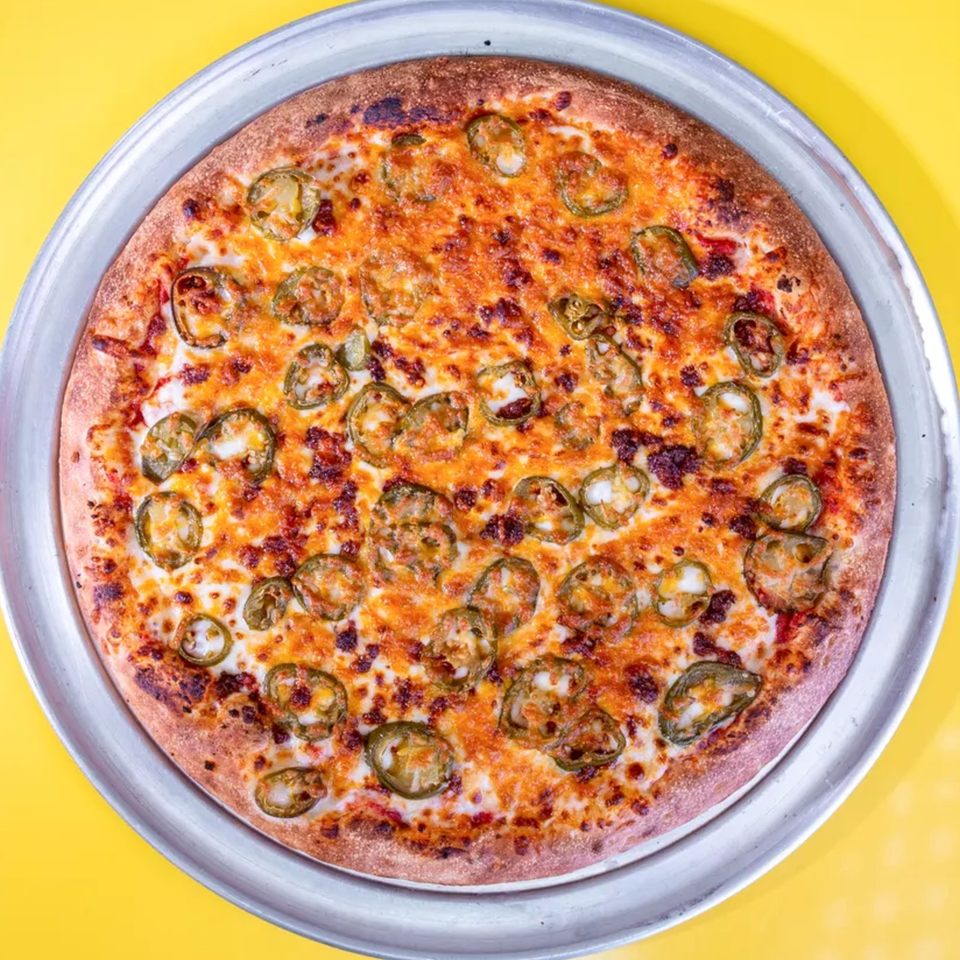 A whole round pizza with melted cheese and sliced jalapeños on a metal pan.
