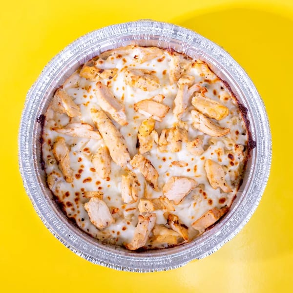 Top-down view of a round foil pan filled with baked pasta, chicken, and melted cheese.